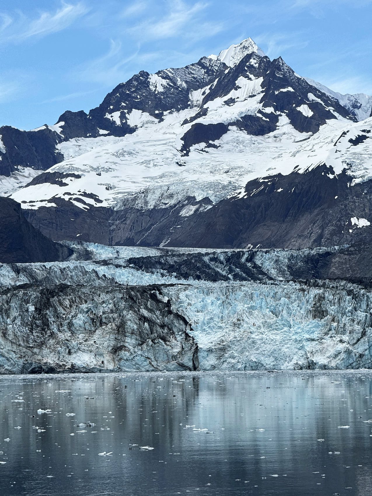 A tidewater glacier meeting calm water beneath snow-capped peaks in Southeast Alaska