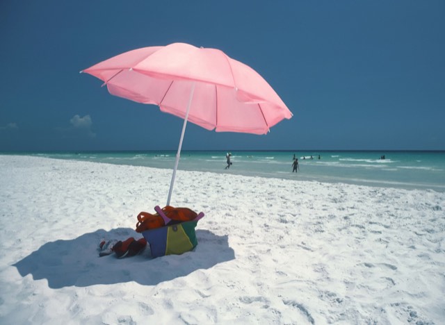 A pink beach umbrella on the brilliant white sand of Seaside beach in South Walton, with emerald-green Gulf water beyond