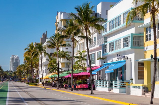 The Ocean Drive streetscape in Miami Beach's Art Deco Historic District — pastel Art Deco hotels, palms, and colorful sidewalk-cafe umbrellas under a blue sky