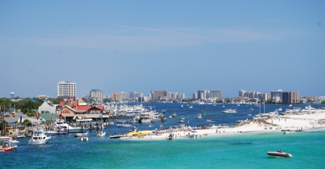 A wide view across Destin Harbor showing the marina and charter-fishing fleet, the turquoise East Pass, and boats off the sandbar