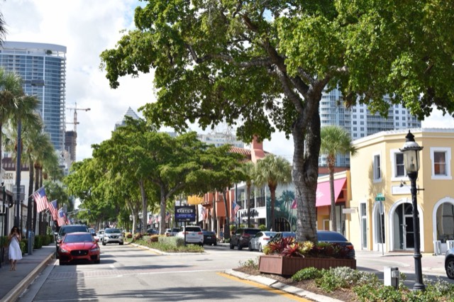 Palm- and tree-lined Las Olas Boulevard in Fort Lauderdale, with low-rise storefronts, awnings, and American flags