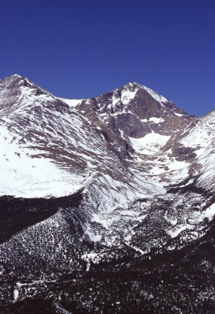 The snow-covered face of Longs Peak rising above the forested valley
