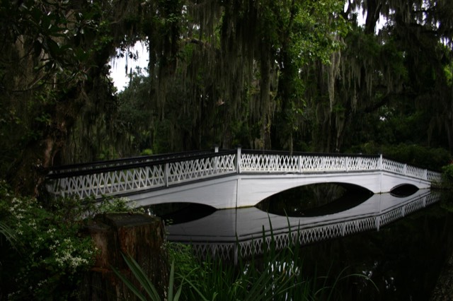 The white lattice footbridge reflected in a dark pond beneath Spanish-moss-draped trees at Magnolia Plantation and Gardens