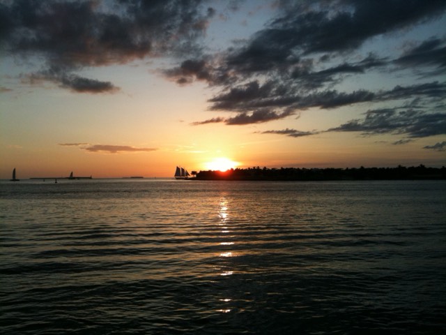 The sun setting over the harbor with a schooner silhouette, viewed from Mallory Square in Key West