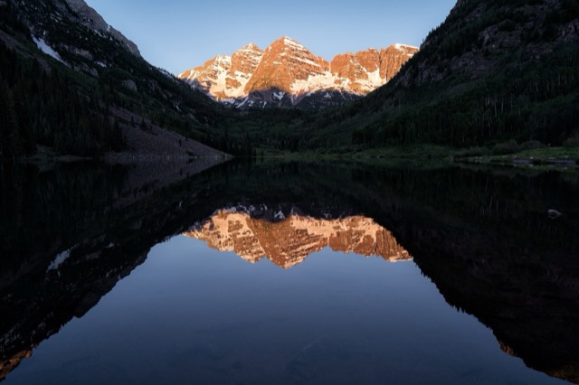 The Maroon Bells at sunrise reflected in the still water of Maroon Lake