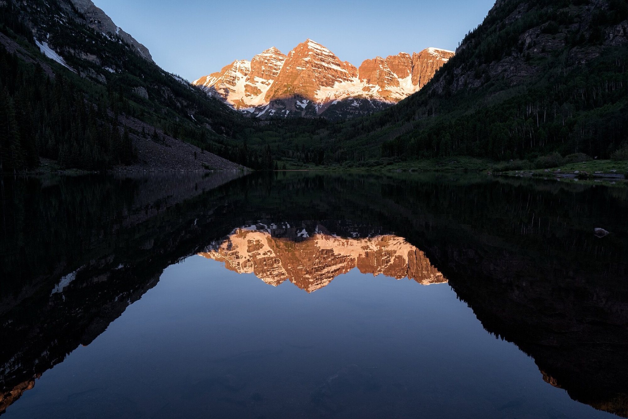 The Maroon Bells at sunrise reflected in the still water of Maroon Lake