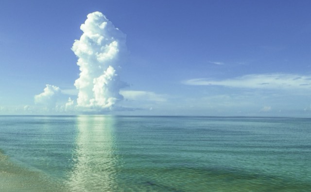 Calm, clear turquoise Gulf water meeting white sand under a towering cumulus cloud at Vanderbilt Beach in Naples