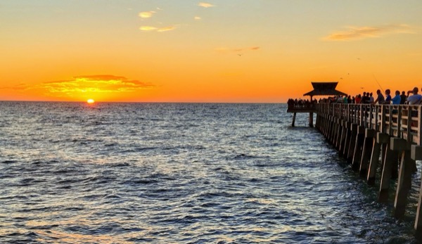 The wooden Naples Pier extending over the Gulf of Mexico as the sun sets on the horizon