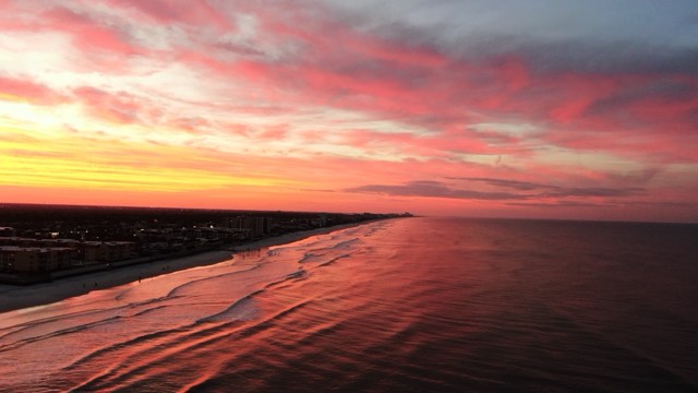 A fiery sunset over New Smyrna Beach, the wet sand mirroring the pink-and-gold sky