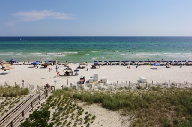 Emerald-green Gulf water meeting white sand at Panama City Beach, with a boardwalk and sea-oat dune in the foreground