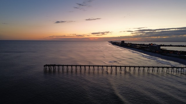 A golden-hour aerial of the Pensacola Beach Gulf Fishing Pier extending into the Gulf of Mexico