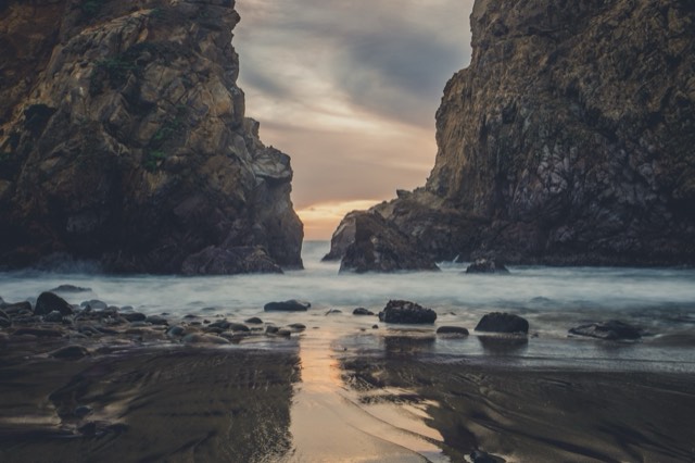The Keyhole Arch at Pfeiffer Beach at sunset, surf glowing through the gap onto wet sand