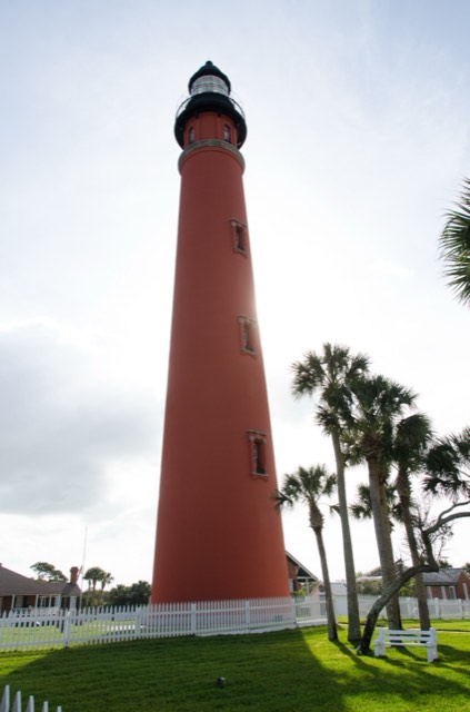 The tall red-brick Ponce de Leon Inlet Lighthouse rising above palms and keeper's houses