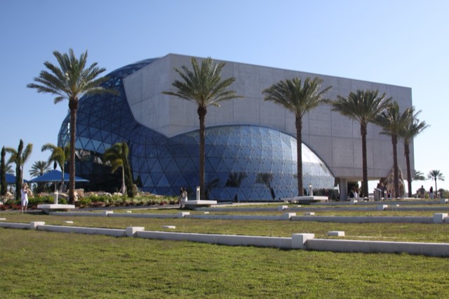 The exterior of The Dali Museum in St. Petersburg, a concrete building with its free-form geodesic glass bubble, the Enigma, fronted by palms