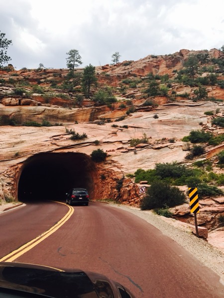 The historic Zion–Mt. Carmel tunnel bored through red slickrock, a car entering the arch