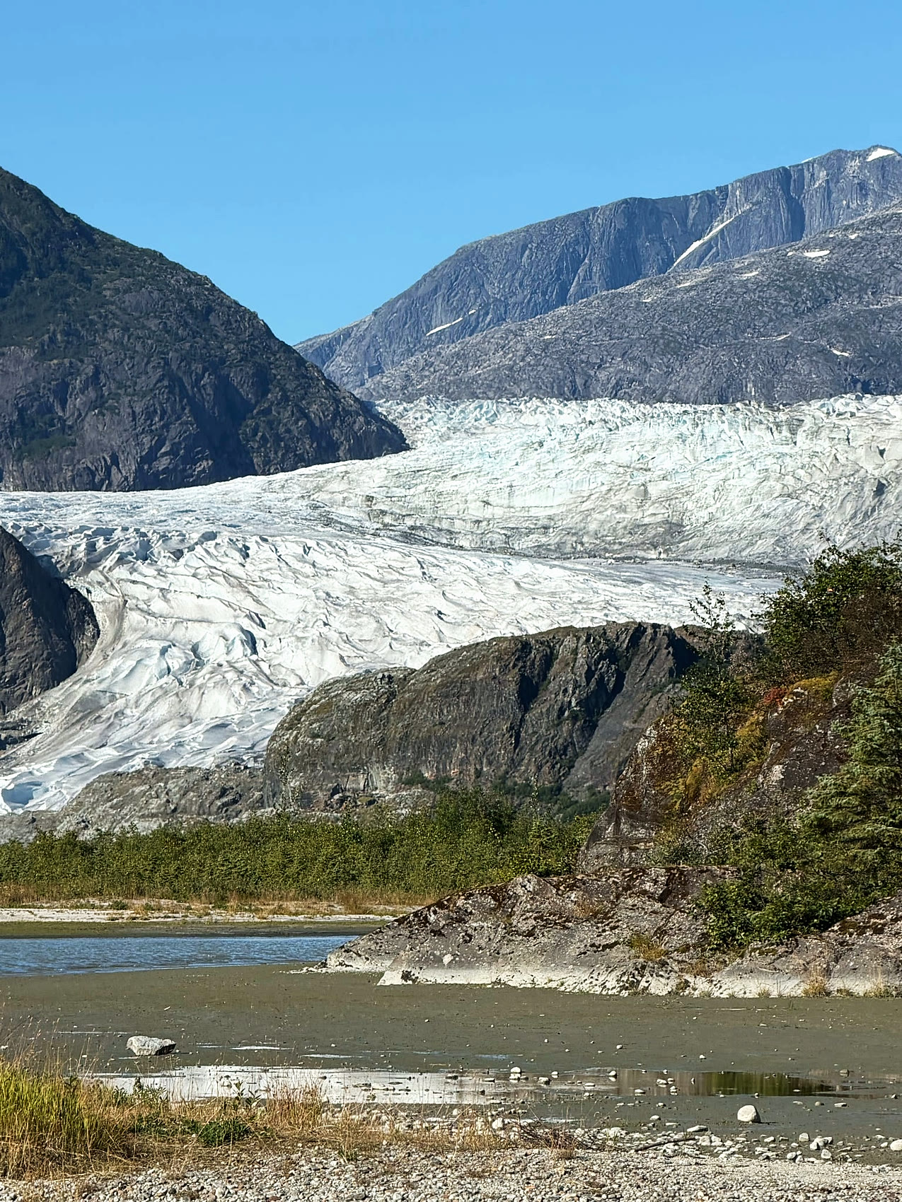 The Mendenhall Glacier flowing down between mountains near Juneau, with the outwash river below