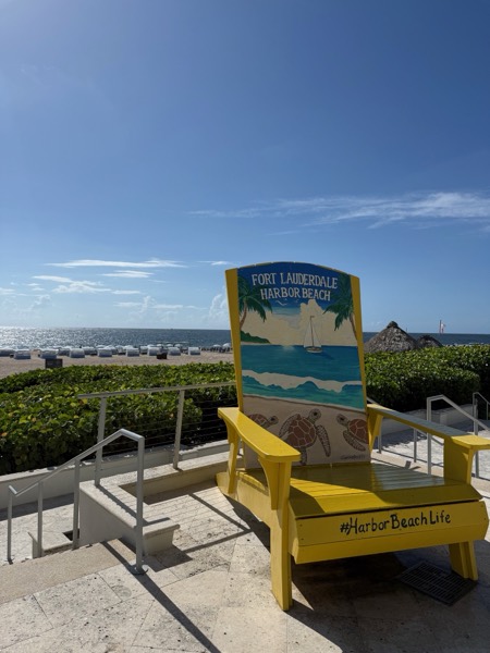 A bright yellow beach chair reading 'Fort Lauderdale Harbor Beach' on the private sand, ocean behind, at the Marriott Harbor Beach Resort