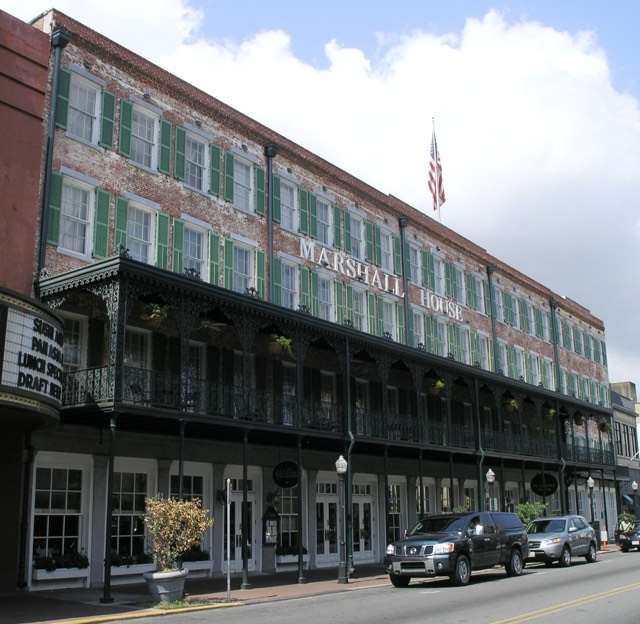 The Marshall House — its 1851 brick facade with green shutters and the signature cast-iron veranda on Broughton Street, Savannah