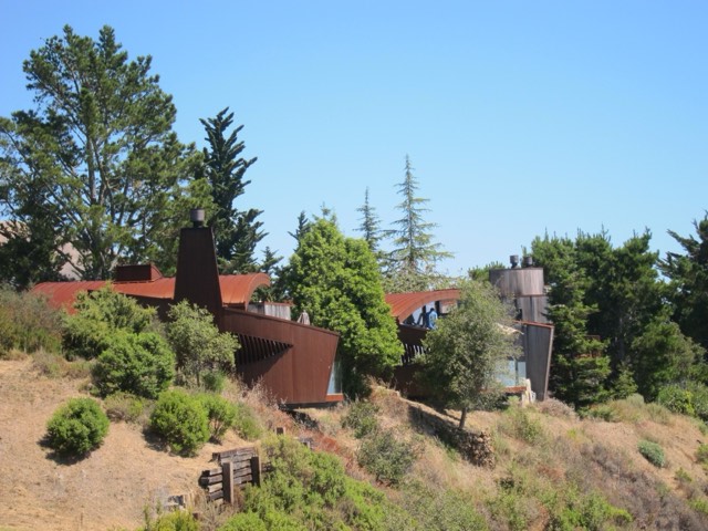 The rusted-steel curved architecture of Post Ranch Inn set into the wooded hillside above the coast