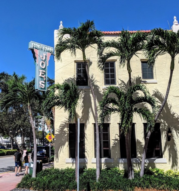Joe's Stone Crab — the historic 1920s Mediterranean building and vintage neon sign framed by royal palms in South Beach